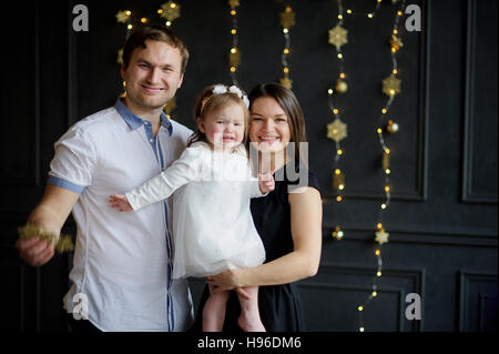 Junge Eltern das weinende Kind zu beruhigen. Der Raum ist festlich geschmückt. Kleines Mädchen weint auf Händen bei Mutter. Baby ist gekleidet in einem weißen Kleid auf dem h Stockfoto