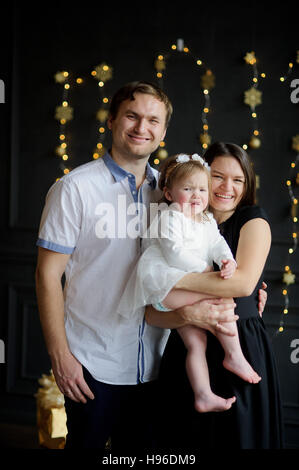 Junge Eltern das weinende Kind zu beruhigen. Der Raum ist festlich geschmückt. Kleines Mädchen weint auf Händen bei Mutter. Baby ist gekleidet in einem weißen Kleid auf dem h Stockfoto