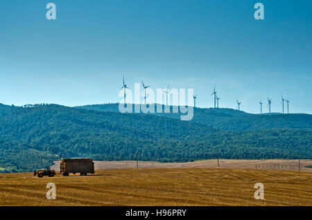 Traktor, die Bearbeitung des Bodens in Piantagini Weizen und im Hintergrund einige Windkraftanlagen Stockfoto