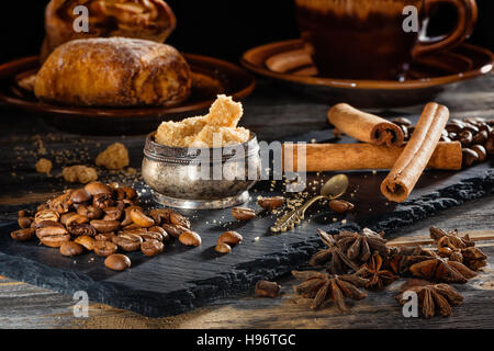 Brauner Zucker, Kaffeekörner und Stangen Zimt auf einer schwarzen Platte aus Schiefer Stockfoto