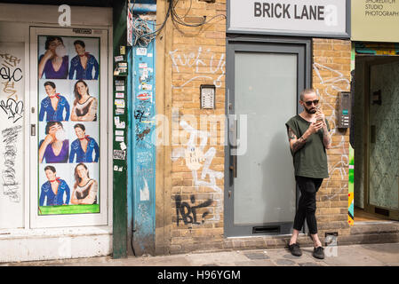 Hipster-Mann mit tätowierten Armen Rauchen einer Zigarette in der Brick Lane, Shoreditch, London, UK. Stockfoto