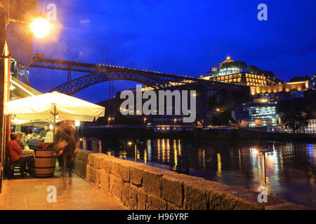 Ein Restaurant am Ufer des Douro, in der Dämmerung mit dem Dom Luis 1 Brücke hinter, in Porto, in Nord-Portugal Stockfoto