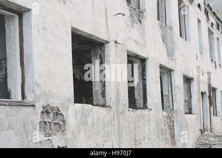 Weiße Wand eines verlassenen Gebäudes. Zerbrochene Fensterscheiben. Stockfoto