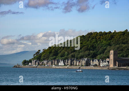 Kirche und Häuser am Fuß eines Hügels mit Wald in der Nähe von dem Fährhafen in Oban, Schottland Stockfoto