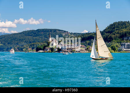 Vintage Holz Segelboot segeln auf See Wörthersee, Kärnten, Österreich. Maria Wörth mit Kirche im Hintergrund. Stockfoto