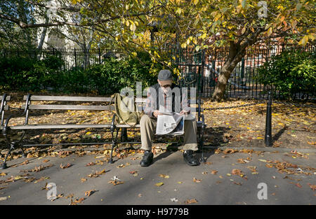 Ein älterer Mann sitzt allein im Washington Square Park im Herbst, die New York Times zu lesen, Stockfoto
