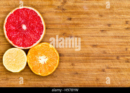 High Angle Stillleben View of geschnittenen Ruby Red Grapefruit, Orange und Zitrone zusammen auf linken Seite des Rahmens auf rustikalem Holzbrett mit angeordnet Stockfoto