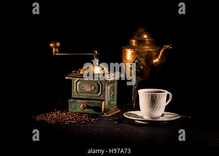 Stillleben mit eine alte Kaffeemühle, Kaffeebohnen, Kaffee-Wasserkocher und eine Kaffeetasse auf einem schwarzen Hintergrund. Stockfoto