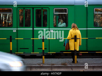 Frau im gelben Mantel und einen grünen Straßenbahn und ein Auto vorbei in Motion blur Stockfoto