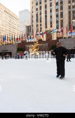 Junger afroamerikanischer Junge, der in der Nähe der Kamera läuft, Eislaufbahn im Rockefeller Center, Prometheus Sculpture von Paul Howard Manship, NYC Stockfoto