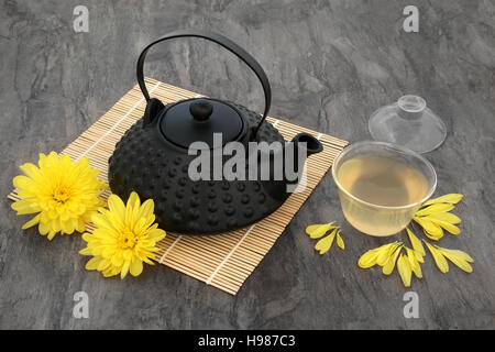 Chrysantheme Blumentee mit Blumen, orientalische Teekanne und Glasschale mit Deckel auf Bambusmatte. Auch verwendet in der traditionellen chinesischen Kräutermedizin. Stockfoto