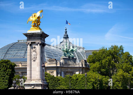 Ansicht des Grand Palais und goldene Statue an der Brücke Pont Alexandre III. Französische Flagge Wellen auf dem Dach des Gebäudes. Blauer Himmel und Bäume sind in der Zeitmessung Stockfoto