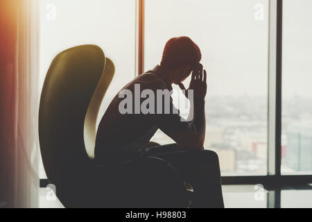 Silhouette der ängstlich und nachdenklich Geschäftsmann im karierten Hemd, auf gelbe Sessel sitzen und schauen in das Fenster der Büroeinrichtung Stockfoto