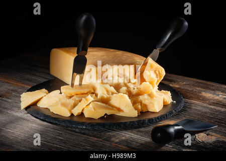 Parmesan Käse mit einem Messer auf Runde Schiefer Board im rustikalen Stil Stockfoto