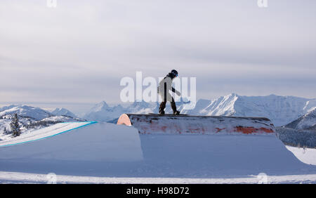 Snowboarder gleiten eine Schiene mit Bergen im Hintergrund Stockfoto