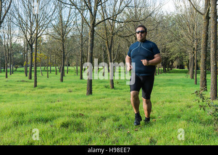 Dicken Bauch Mann Joggen, Sport treiben, tun, Cardio im Park, leicht übergewichtig, Gewicht zu verlieren. Auf einer Wiese grüne Gras zwischen den Bäumen ohne lea Stockfoto