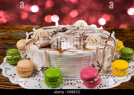 Kuchen für Silvester mit Macarons auf Schreibtisch aus Holz, hell rosa und rote Lichter auf Hintergrund, Neujahr-Konzept Stockfoto