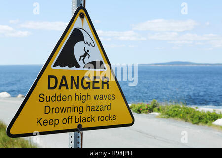 Ein Schild warnt vor plötzlichen hohen Wellen an Peggys Punkt, neben der Küste Dorf von Peggys Cove in Nova Scotia, Kanada. Stockfoto