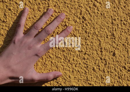 Eine Hand auf eine gelbe körnige Wand Stockfoto