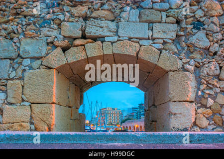 Die Lücke in der Steinmauer auf venezianischen Festung öffnet sich der Blick am Abend Hafen mit Segel Yachten und Stadtgebäude, Heraklion, Kreta, Griechenland. Stockfoto