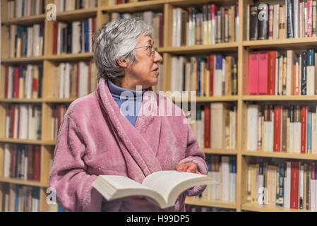 Ältere Frau im Hintergrund verschwommen Bibliothek ein Buch auswählen. Stockfoto