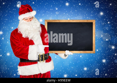 traditionelle klassische rote weiße Weihnachtsmann macht zeigte mit seinem Finger auf hölzerne Tafel Plakatwand in seiner anderen Hand isoliert vor der blauen nig Stockfoto