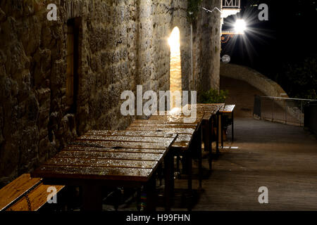 Nass, leer, hölzerne Tische in der Nacht auf schmalen Durchgang in der Stadt San Gimignano in der Toskana, Italien. Stockfoto