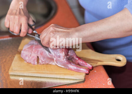 Ältere Frau Hände schneiden roh Kaninchen Fleisch auf einem Wodden Tisch. Flachen Dof, selektiven Fokus an Hand der Frau. Stockfoto