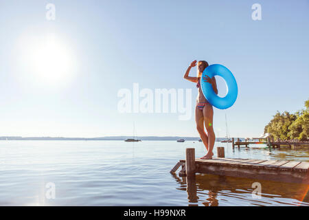 Junge Frau steht auf Pier See mit aufblasbaren ring Stockfoto