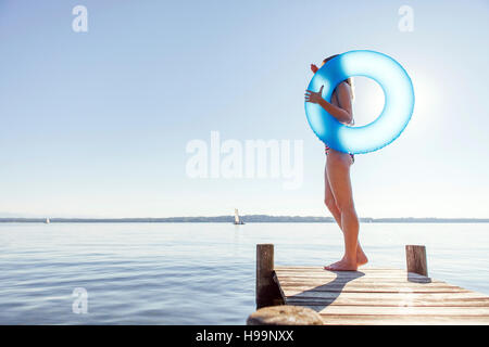 Junge Frau steht auf Pier See mit aufblasbaren ring Stockfoto