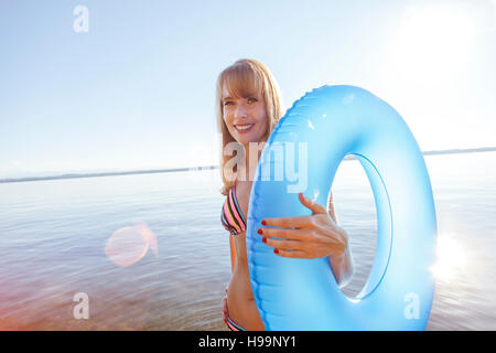 Junge Frau steht auf Pier See mit aufblasbaren ring Stockfoto