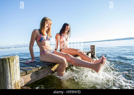 Junge Frauen sitzen auf Pier Spritzwasser mit Beinen Stockfoto