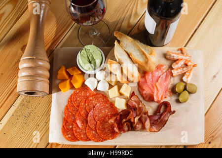 Antipasti-Platte auf der Holzoberfläche. Flasche und Glas Wein. verschiedene Snacks. Stockfoto