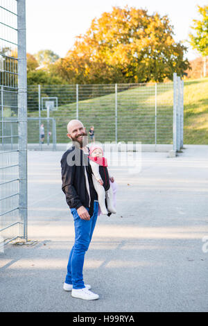 Vater mit Babymädchen in Babytrage auf Spielfeld Stockfoto