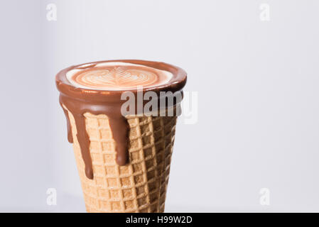 Kaffee im Waffelhörnchen in Schokolade getaucht, mit Zeichnungen in Cappuccino / Latte Milchschaum, Latte Art, isoliert Stockfoto