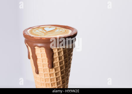 Kaffee im Waffelhörnchen in Schokolade getaucht, mit Zeichnungen in Cappuccino / Latte Milchschaum, Latte Art, isoliert Stockfoto