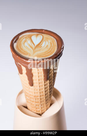 Kaffee im Waffelhörnchen in Schokolade getaucht, mit Zeichnungen in Cappuccino / Latte Milchschaum, Latte Art, isoliert Stockfoto