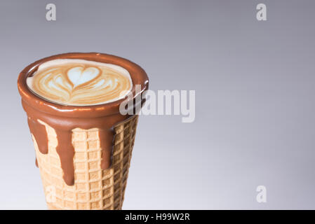 Kaffee im Waffelhörnchen in Schokolade getaucht, mit Zeichnungen in Cappuccino / Latte Milchschaum, Latte Art, isoliert Stockfoto
