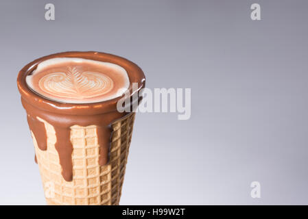 Kaffee im Waffelhörnchen in Schokolade getaucht, mit Zeichnungen in Cappuccino / Latte Milchschaum, Latte Art, isoliert Stockfoto