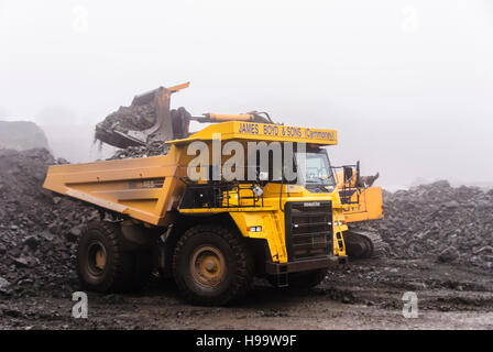 Ein Broyt verfolgt Loader lädt ein Kubota-465-Rock-Muldenkipper in einem Steinbruch bei starkem Regen. Stockfoto