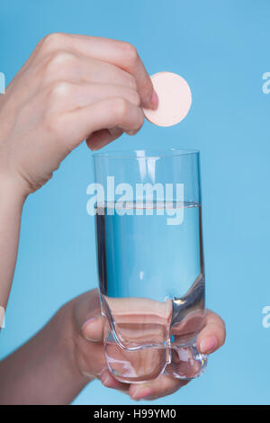 Vitamine, Gesundheit, Medikamente. Person werfen Vitamin Mineral ergänzen Brausetablette in einem Glas Wasser. Studio gedreht auf blauem Hintergrund Stockfoto