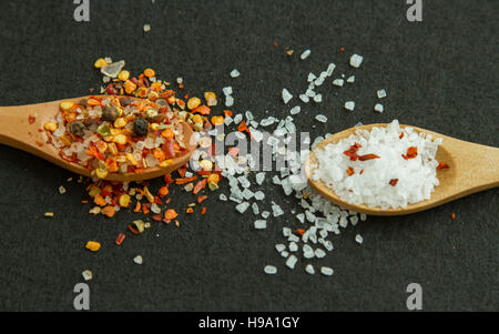 Zwei hölzerne Löffel mit Gewürzen und Salz auf schwarzem Hintergrund Stockfoto