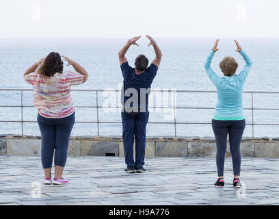 Reifer Mann und zwei Reife Frauen praktizieren Tai Chi mit Blick aufs Meer Stockfoto