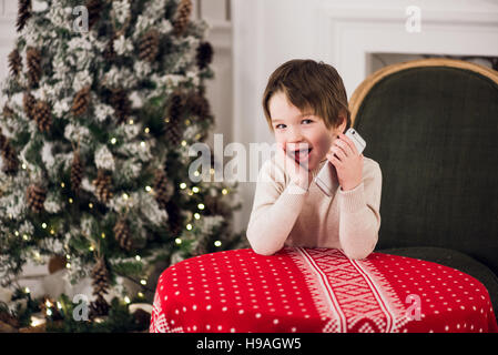 junge ruft Santa beim Sitzen auf einem großen grünen Sessel zu Hause über Chirstmas Baum Hintergrund Stockfoto