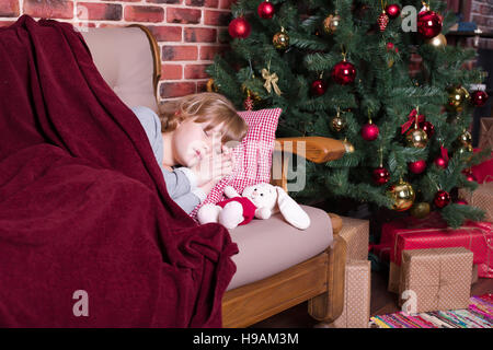 Mädchen schläft unter einer Decke auf dem Sofa in der Nähe der Weihnachtsbaum mit Geschenken Stockfoto