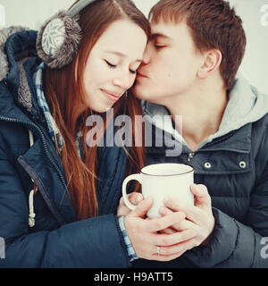 Liebespaar in warme Kleidung trinken Heißgetränk im Freien im Winter, Mann Frau küssen Stockfoto