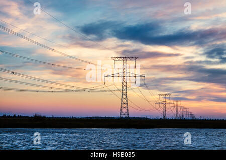 Hochspannungsleitungen über Fluss bei Sonnenuntergang Stockfoto