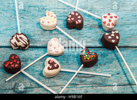 viele Cake Pops in Form Herzen liegen auf der alten blauen hölzernen Hintergrund Draufsicht. Stockfoto