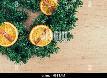 Tannen-Kranz ist mit Orange und Zimt auf einem hölzernen Hintergrund dekoriert. Stockfoto