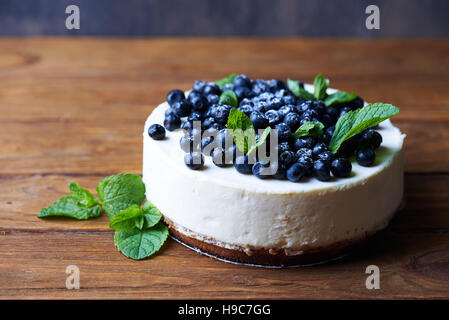 Süße cremige Heidelbeeren Käsekuchen mit frischen Blaubeeren und Minze Blätter auf einem hölzernen Hintergrund mit Textfreiraum. Stockfoto